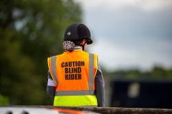 A para dressage rider wearing a white band on the upper arm and a fluorescent vest which says 'caution blind rider'.